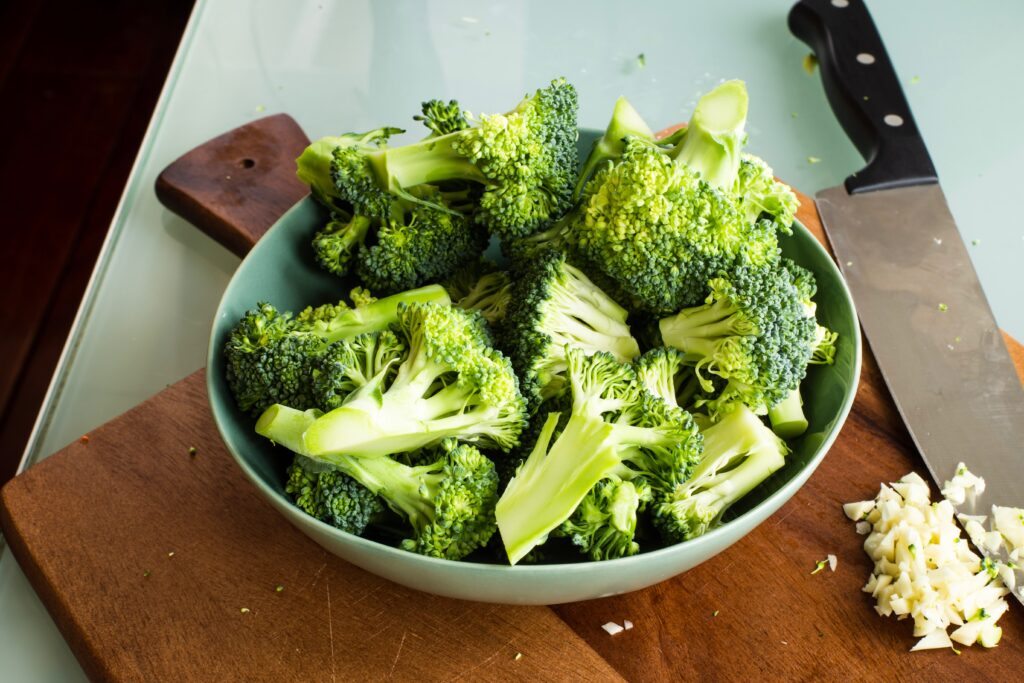 Bowl of Broccoli on wood cutting board next to a chef knife