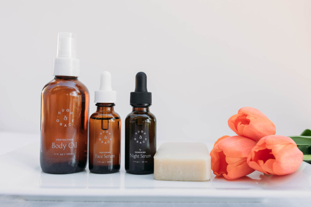 Body oil, face serum and night serum on counter with three pink tulips