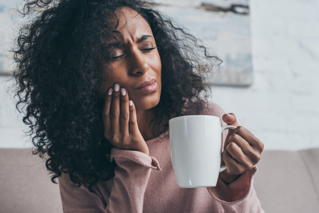 Woman holding side of face with tooth pain while holding a cup of coffee