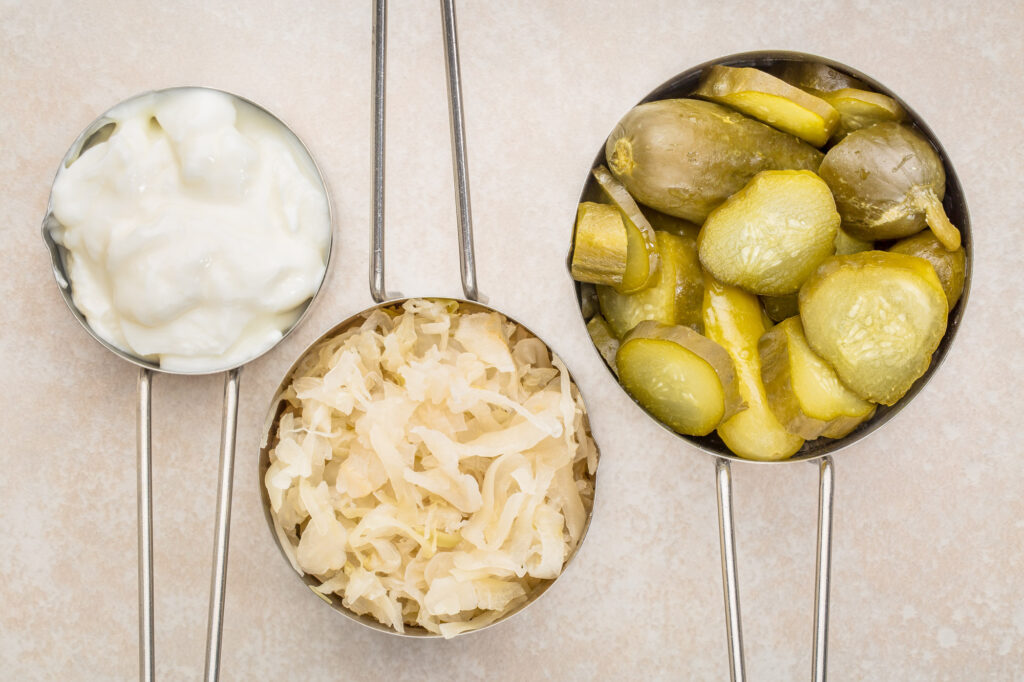Scoops of each yogurt sauerkraut and pickles on beige counter