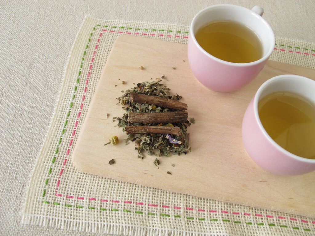 Two pink cups sitting on placemat with licorice root and herbal tea
