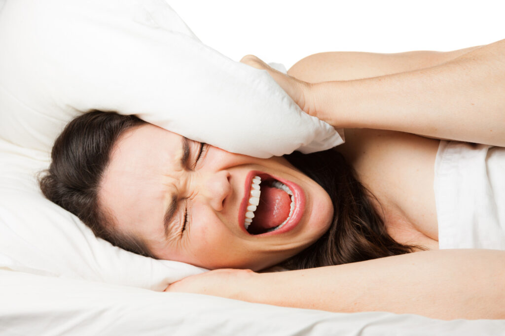 Woman on white bed unable to sleep and screaming with pillow over head