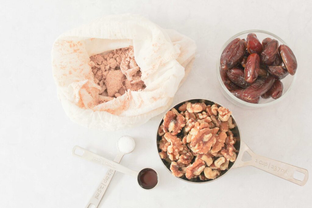 almond pulp granola ingredients showing dates, walnuts, almond pulp, salt and vanilla extract on white counter