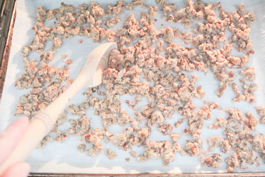 hand stiring almond pulp granola with wooden spoon while baking in oven