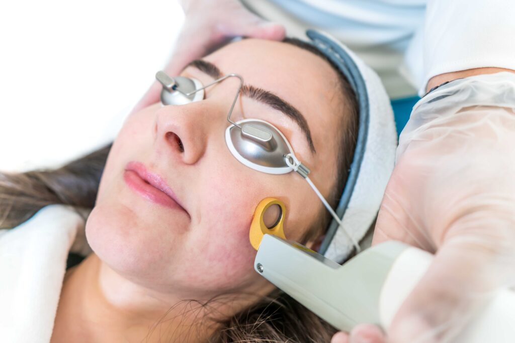 Woman with eye protection receiving laser treatment on face at doctors office