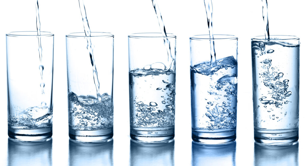 5 glasses of water with stream of water being poured into each with white background