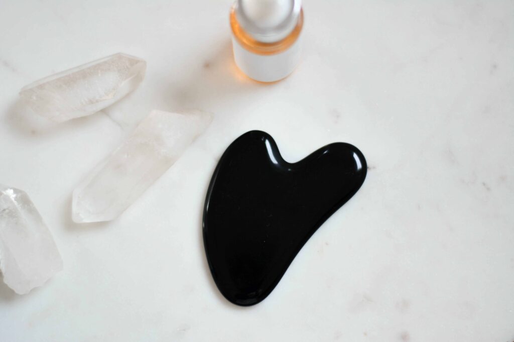 Black Gua Sha Stone on white counter with crystals and face serum for gua sha