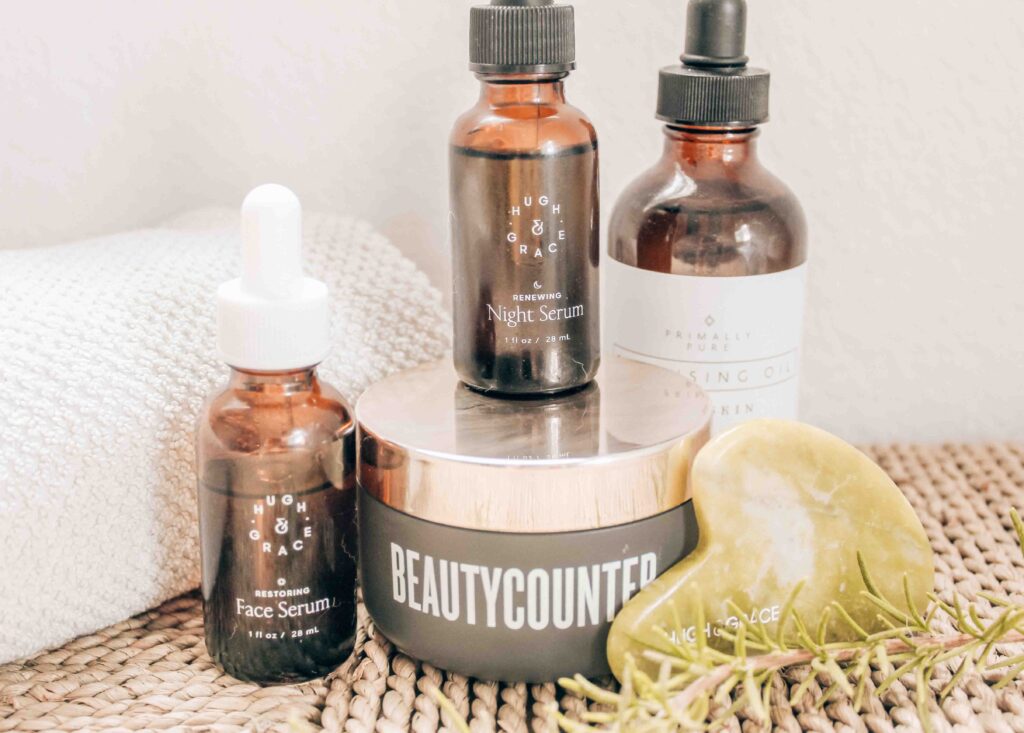 Hugh and Grace, Primally Pure and Beautycounter oils sitting on wicker table with white towel and Hugh and Grace Gua Sha stone
