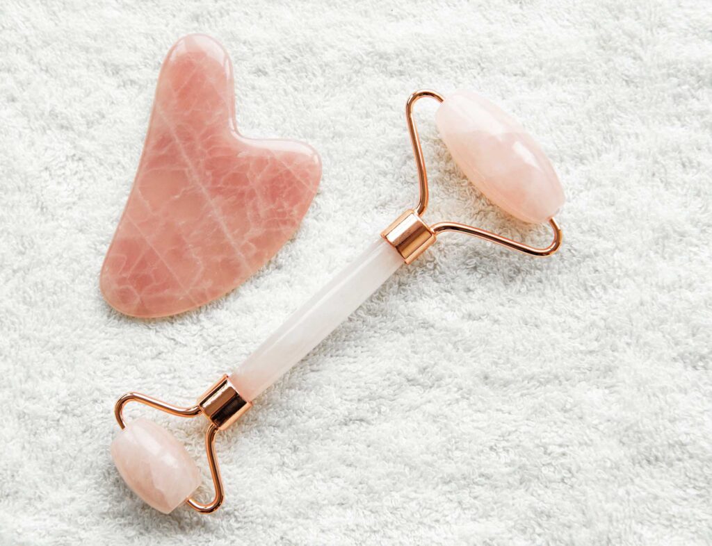 Pink rose quartz jade roller and gua sha stone on white fluffy towel