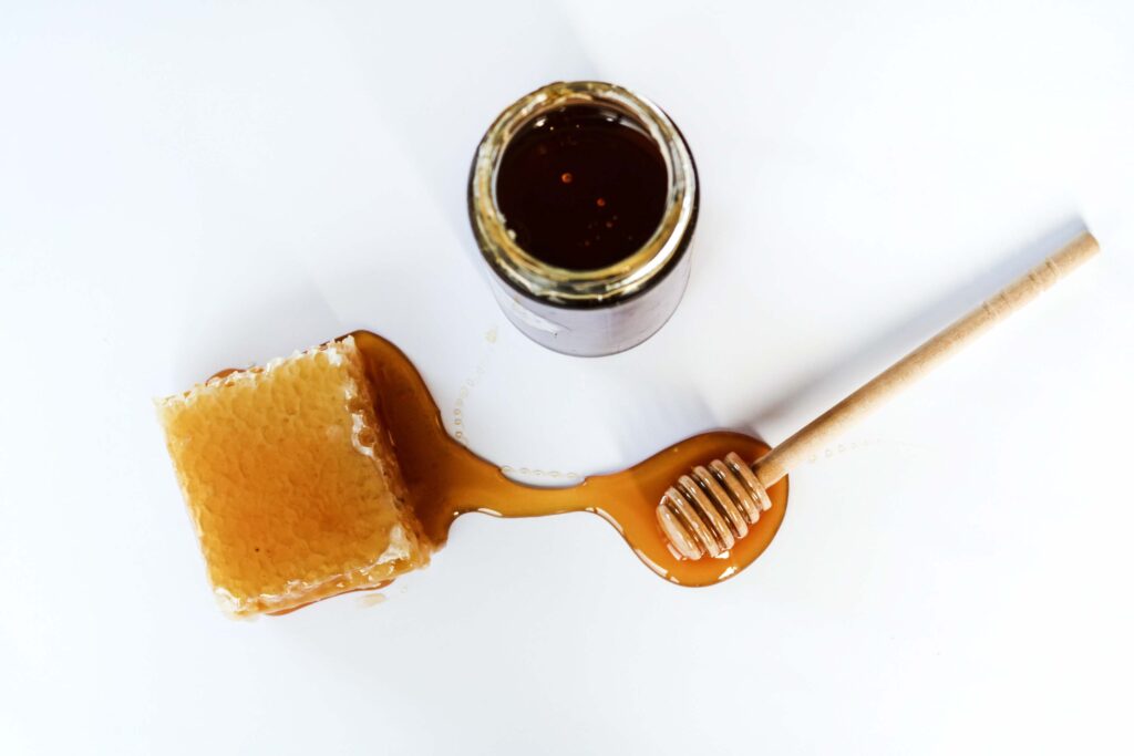 Jar of honey with honeycomb and honey scoop on white counter with honey spilled