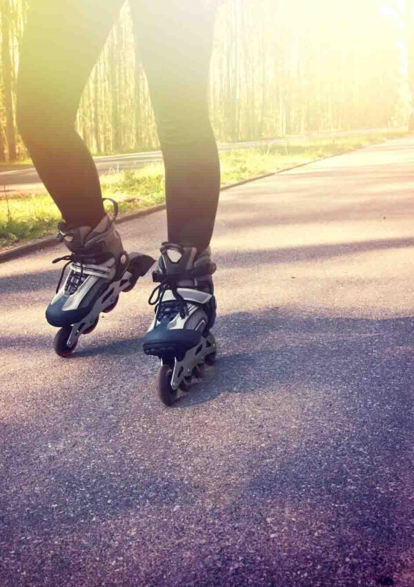 zoom in on woman wearing rollerblades skating on asphalt road surrounded by trees