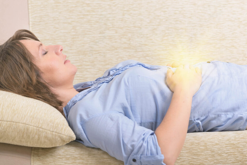 Woman practicing self Reiki transfering energy through palms while laying on couch