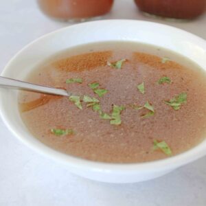 chicken bone broth in white bowl on white counter with mason jars of bone broth in background