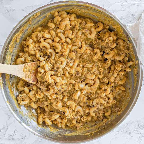 fresh made dairy free cheeseburger macaroni in stainless steel pan, ready to serve with wooden spoon