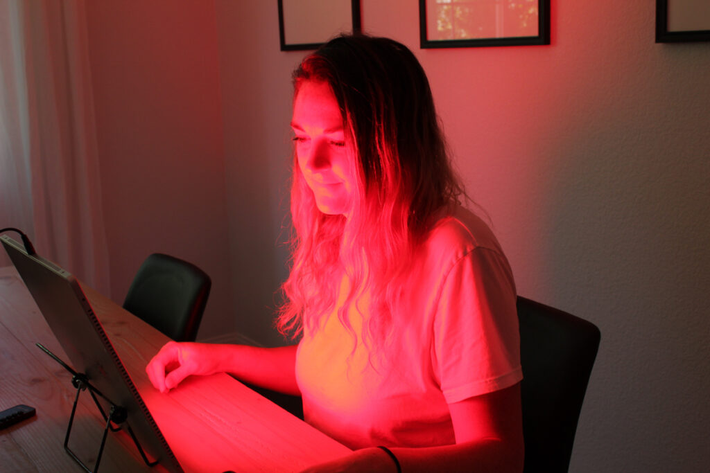 woman sitting at table with TrueLight red light therapy device shining on face and chest