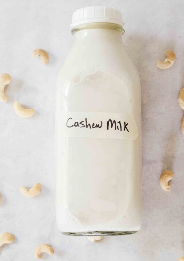 cashew milk bottle with masking tape "cashew milk" label sitting on concrete countertop with raw cashews around