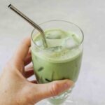 hand holding glass of iced matcha latte with a metal straw