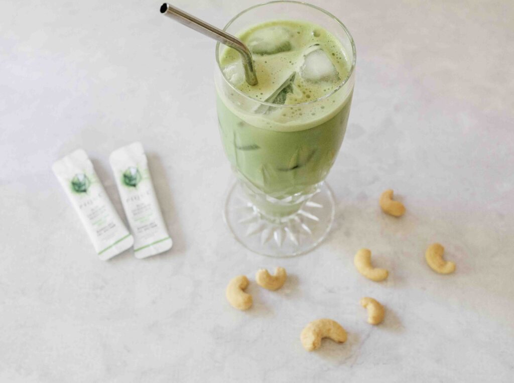 Iced matcha latte on concrete counter with a metal straw and cashews and pique tea packets on counter