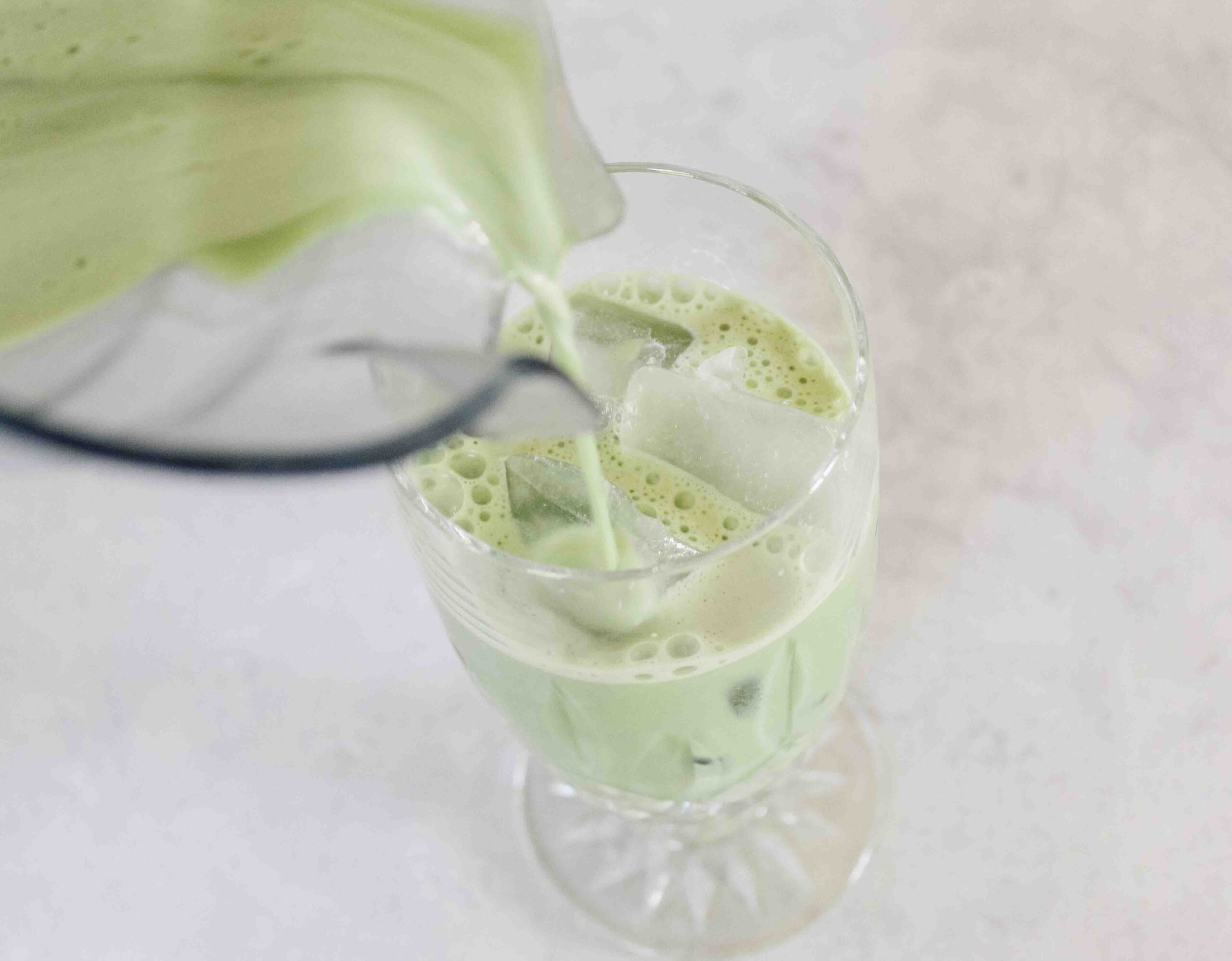 Iced matcha latte being poured from blender into a cup of iced