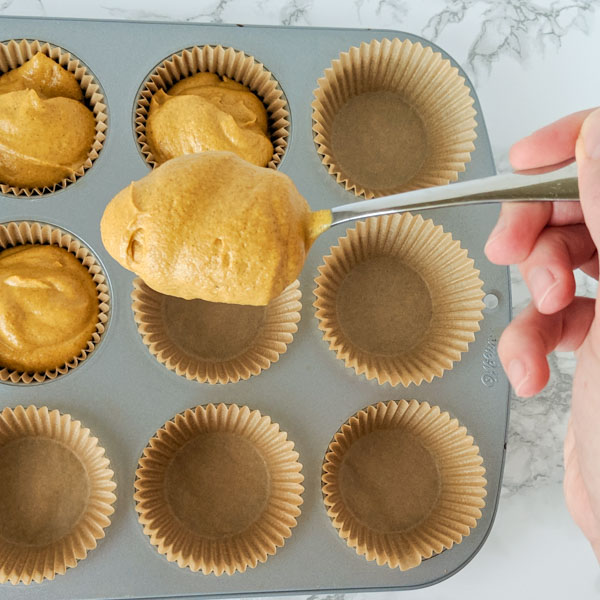 Hand holding a spoon with paleo pumpkin muffin batter being placed into lined muffin pan