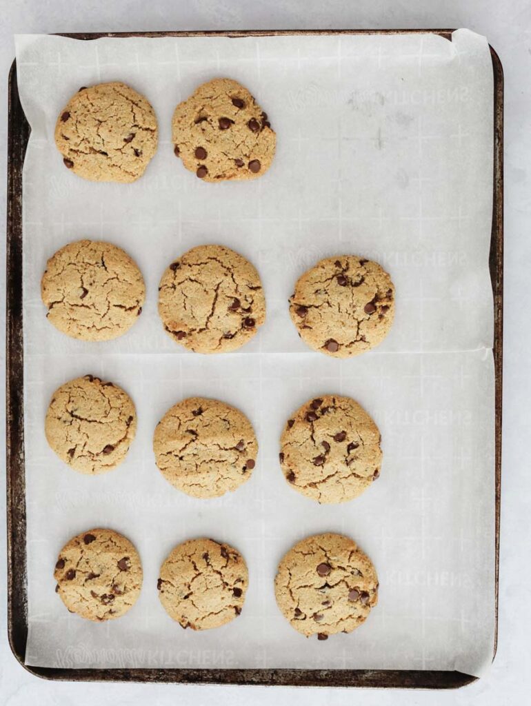 fresh baked dairy free chocolate chip cookies on parchment paper lined baking sheet with one missing