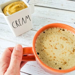 coffee with pumpkin spice coffee creamer in an orange mug on a wood table with creamer in background