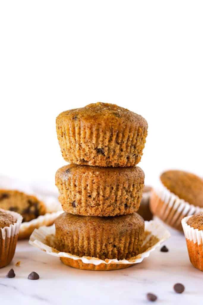 Stacked gluten-free chocolate chip muffins on counter with chocolate chips.