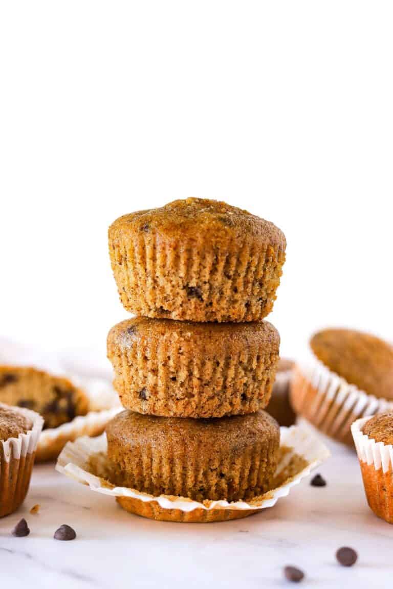 Stacked gluten-free chocolate chip muffins on counter with chocolate chips.
