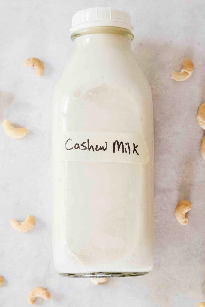 Homemade cashew milk labeled on counter with cashews surrounding bottle.