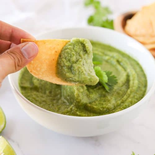 Hand dipping a corn tortilla chip into a bowl of fresh nightshade free salsa.