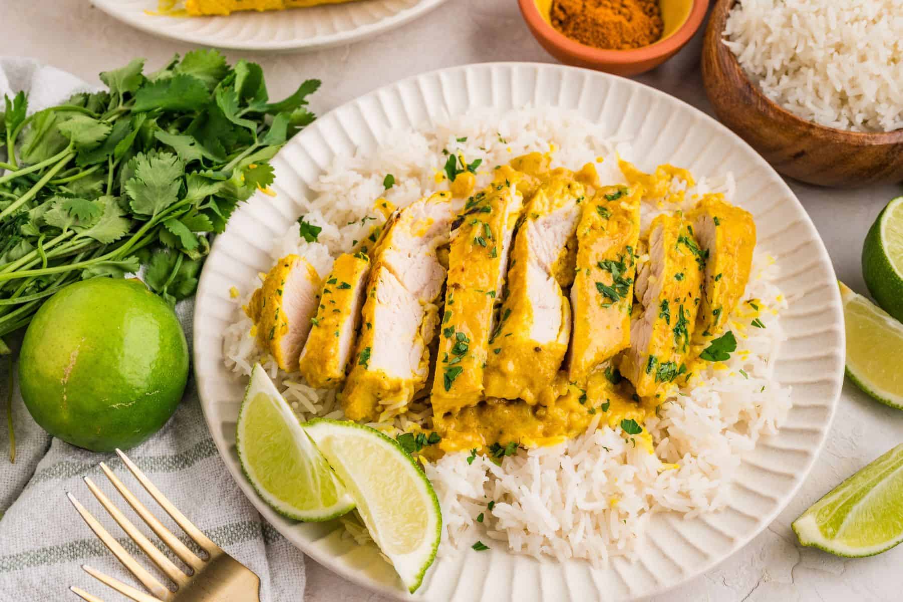 Braised coconut chicken breast cut into slices and served over rice on plate.
