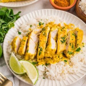 Braised coconut chicken breast served over white rice on plate.