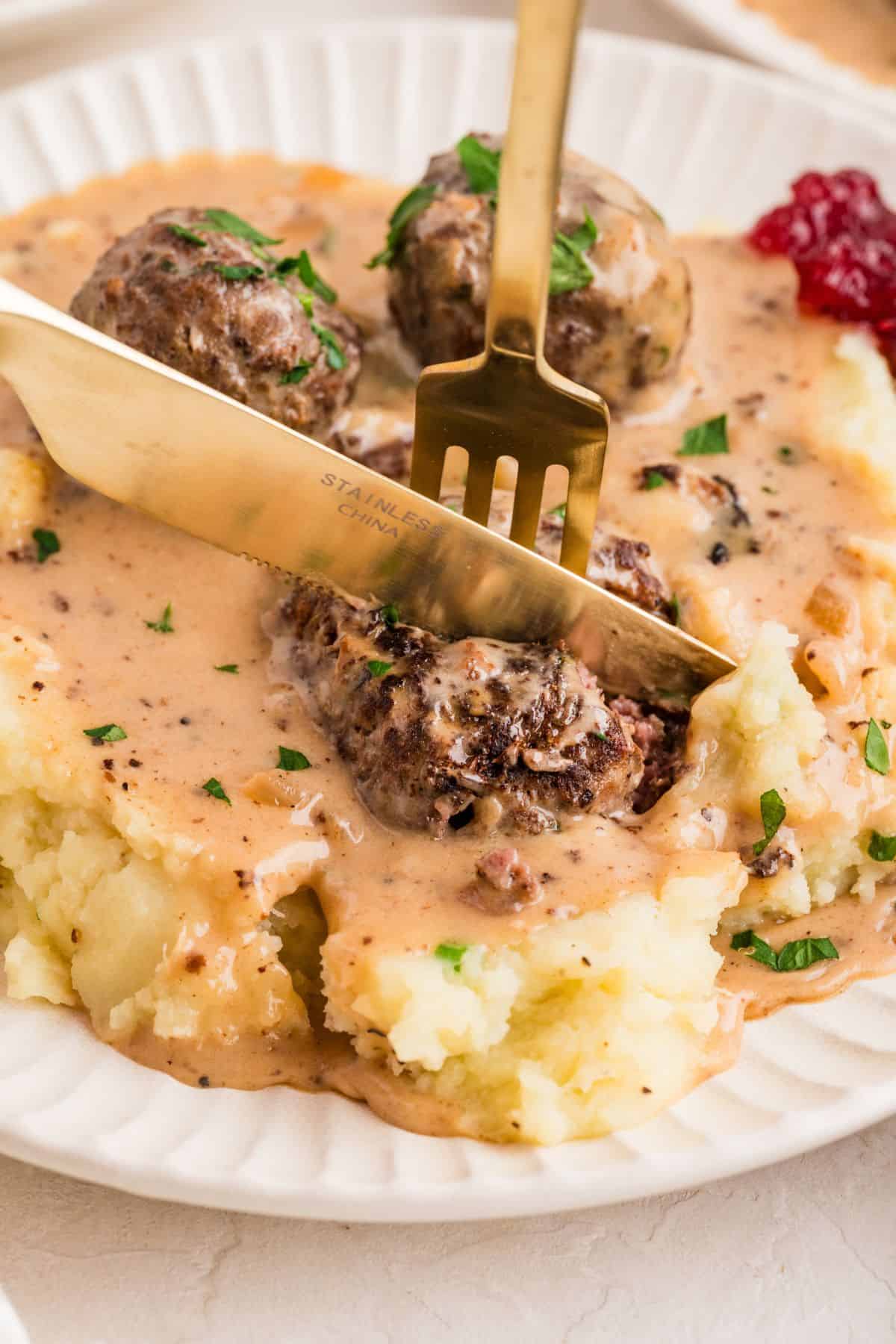 Cutting into dairy free swedish meatballs served over sides on plate.