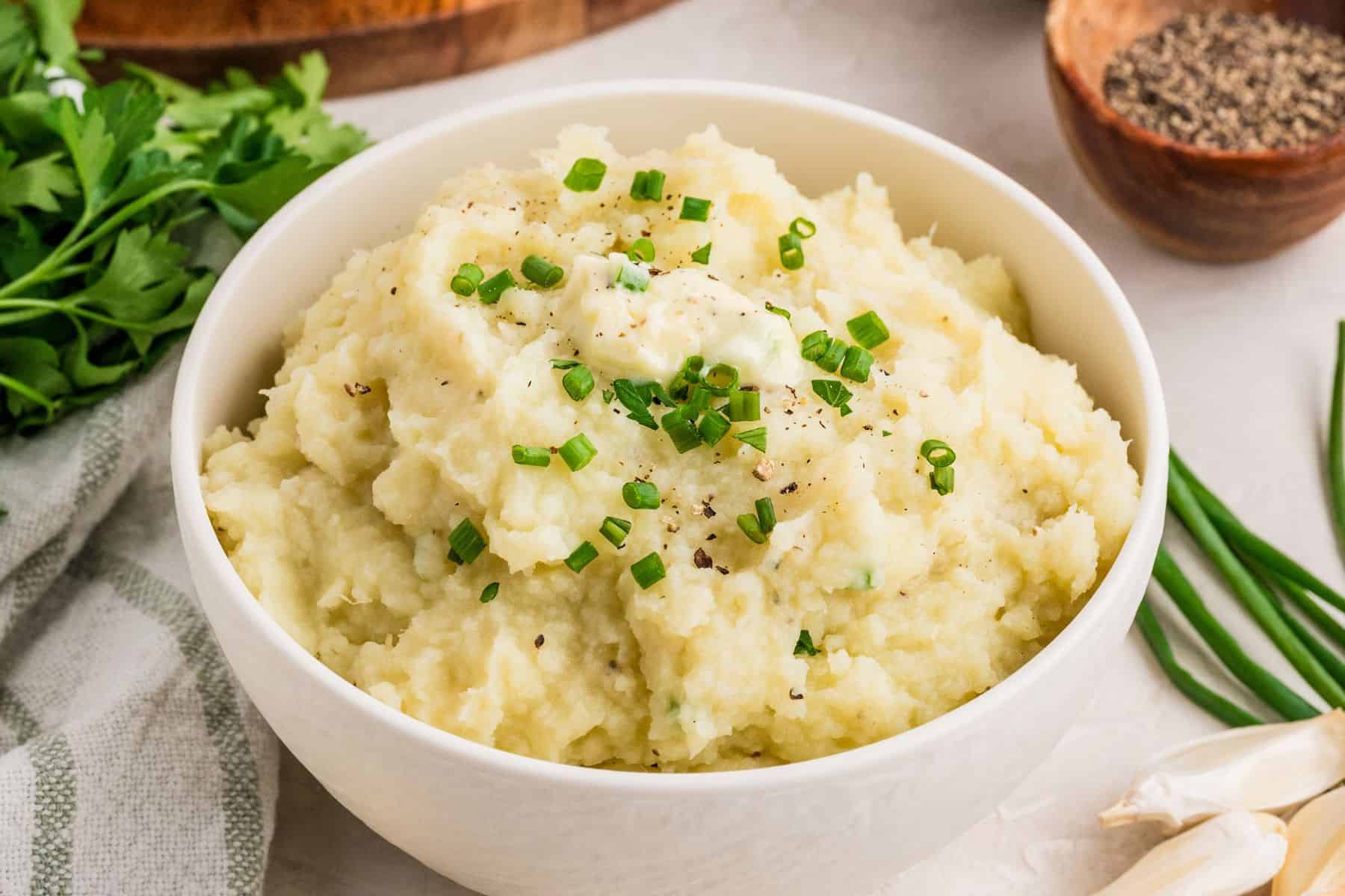 Mashed white sweet potatoes in a serving bowl topped with diced chives and black pepper.