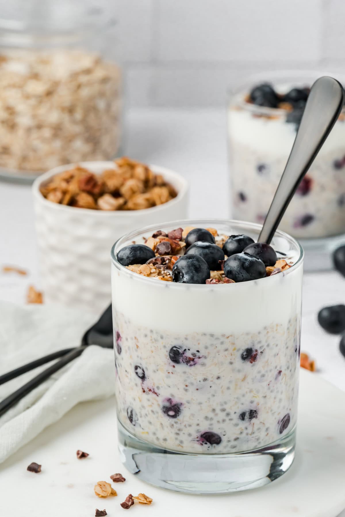 Blueberry overnight oats topped with granola, yogurt and fresh blueberries, in a small cup with a spoon ready for serving.