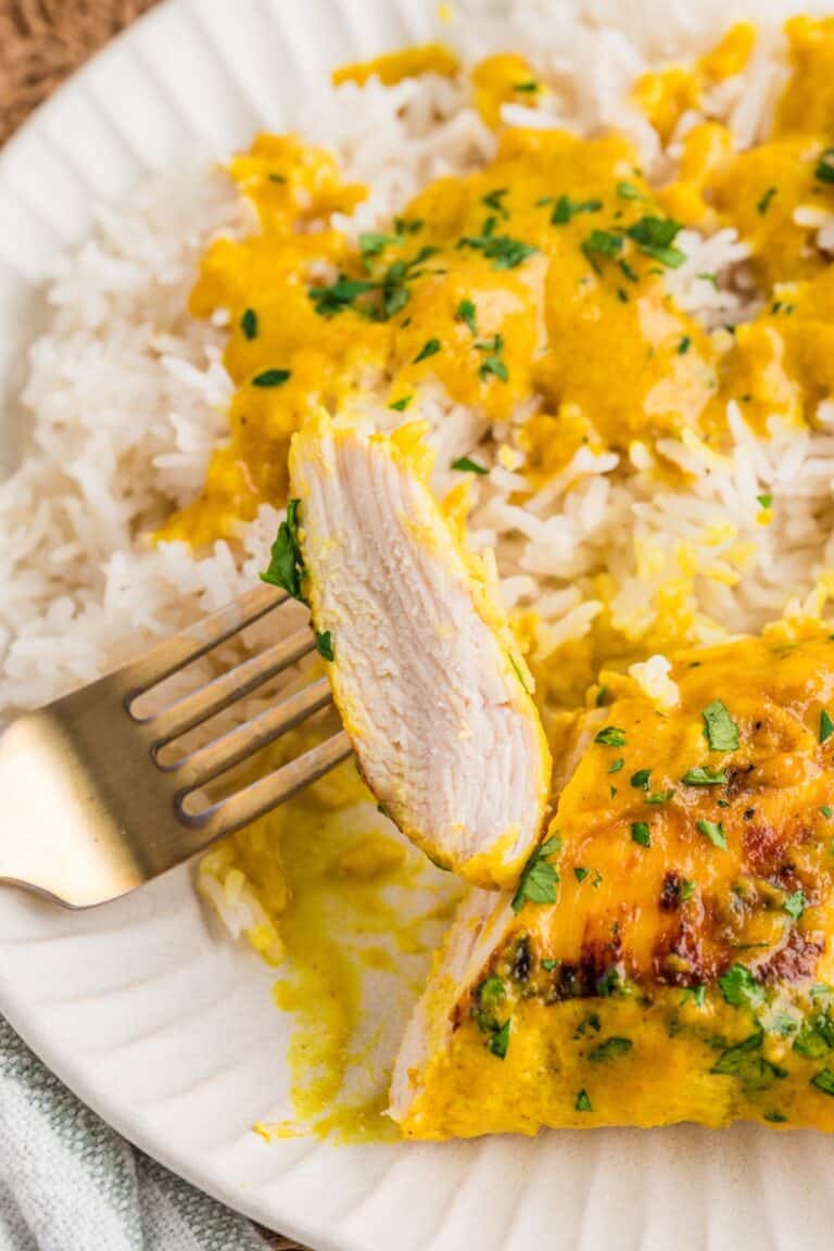 A slice of braised coconut chicken breast on a fork while plated with steamed rice.