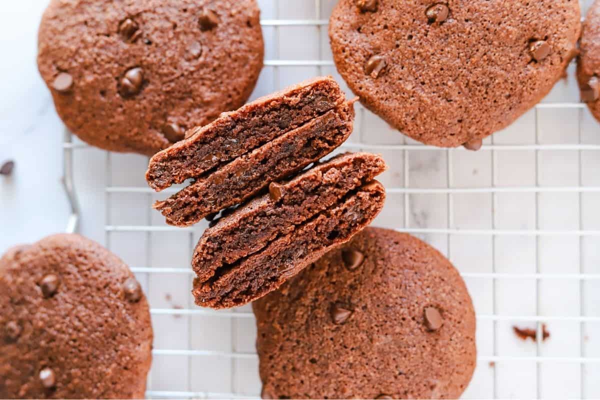 Gluten free double chocolate chip cookies on a wire rack with a focus on two cookies broken open to show texture.