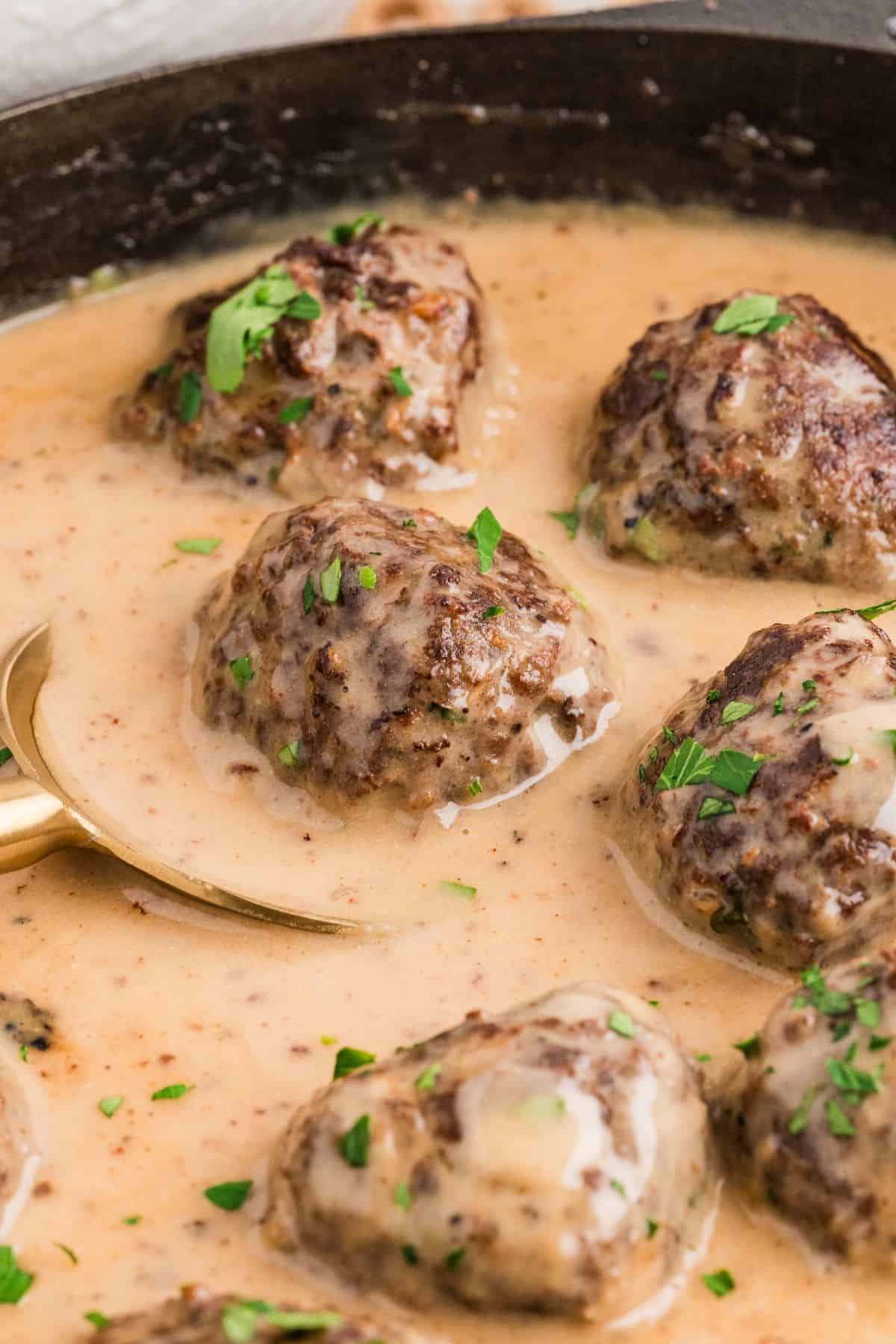 Close up of spoon scooping out a dairy free Swedish meatball with gravy for serving.