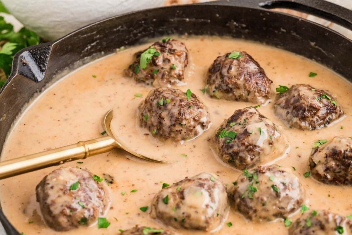 Gluten and dairy free Swedish meatballs in sauce in a large skillet being scooped out of skillet for serving.