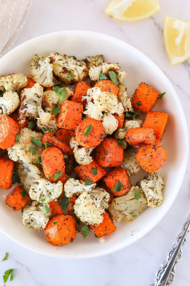Roasted carrots and cauliflower with fresh herbs on top in a serving bowl.