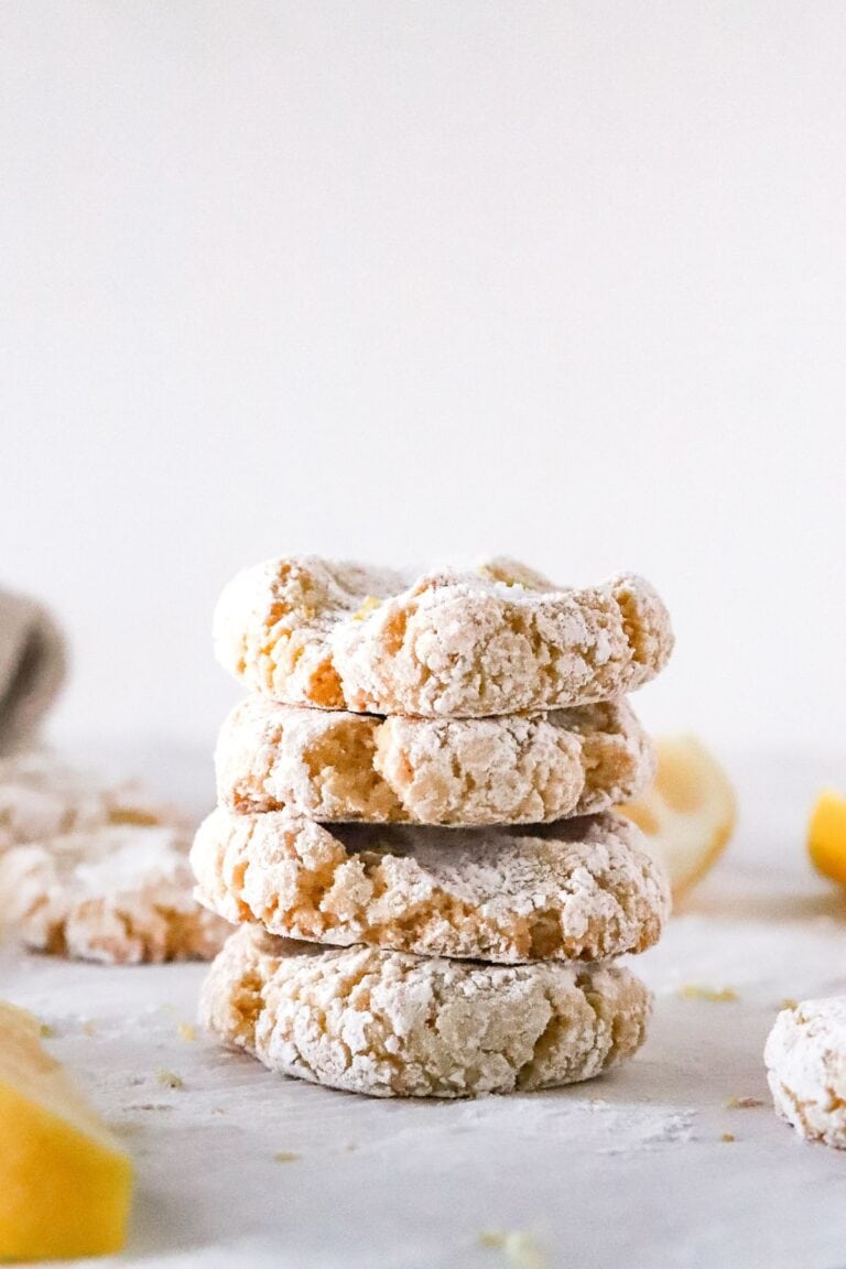 Four gluten free lemon cookies stacked on a piece of parchment paper to show cookie thickness.