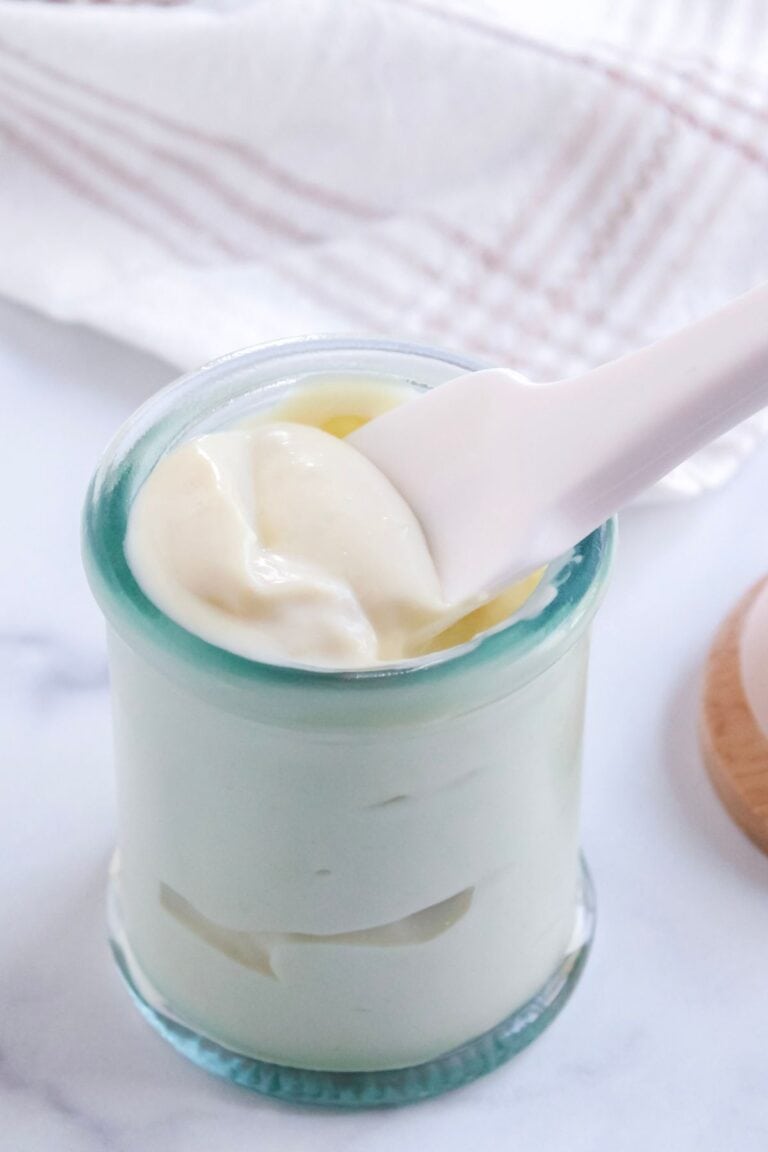 Avocado oil mayo in a jar with lid off sitting on counter with a silicone spoon inside jar.