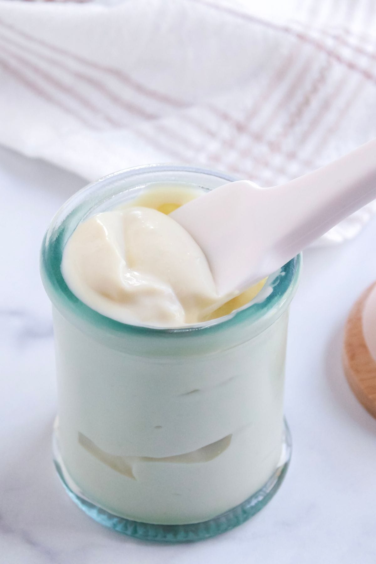 Avocado oil mayo in a jar with lid off sitting on counter with a silicone spoon inside jar.