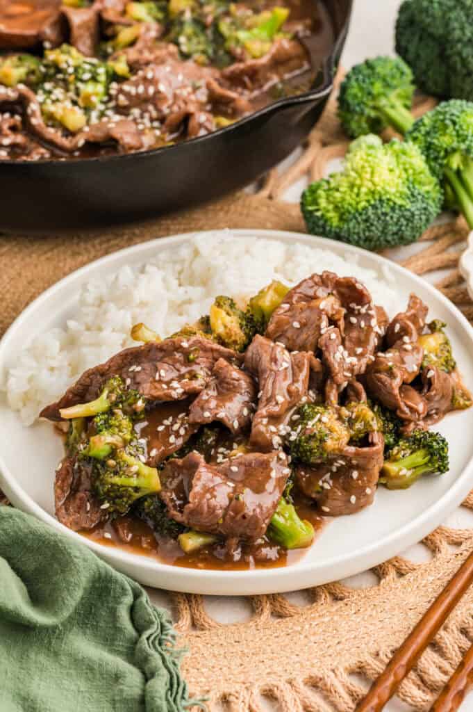 gluten free beef and broccoli on a plate for serving with white rice and the skillet in the background.