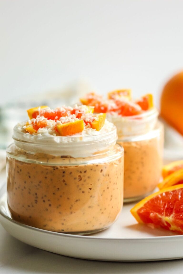 Two jars of dairy free orange cream chia pudding on a plate topped with orange pieces and dairy free yogurt.