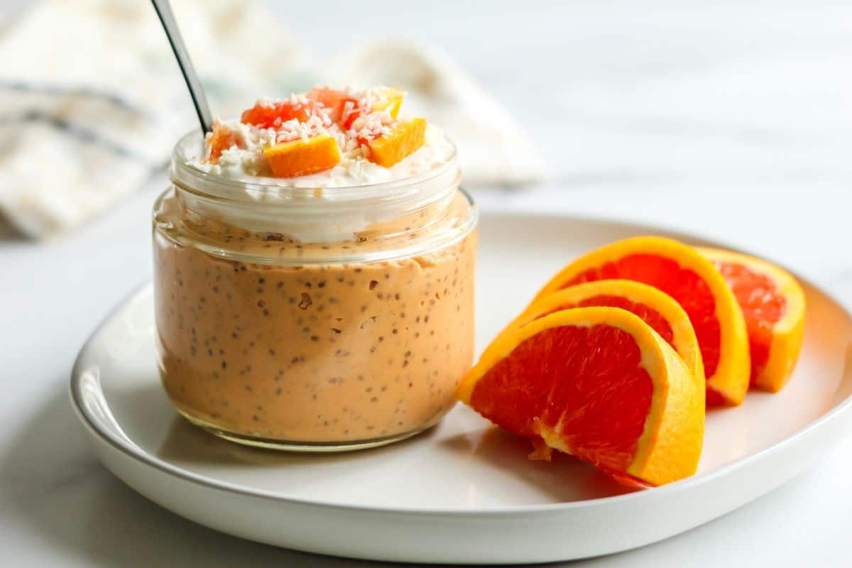 A jar of dairy free orange chia pudding on a plate with orange slices for serving.