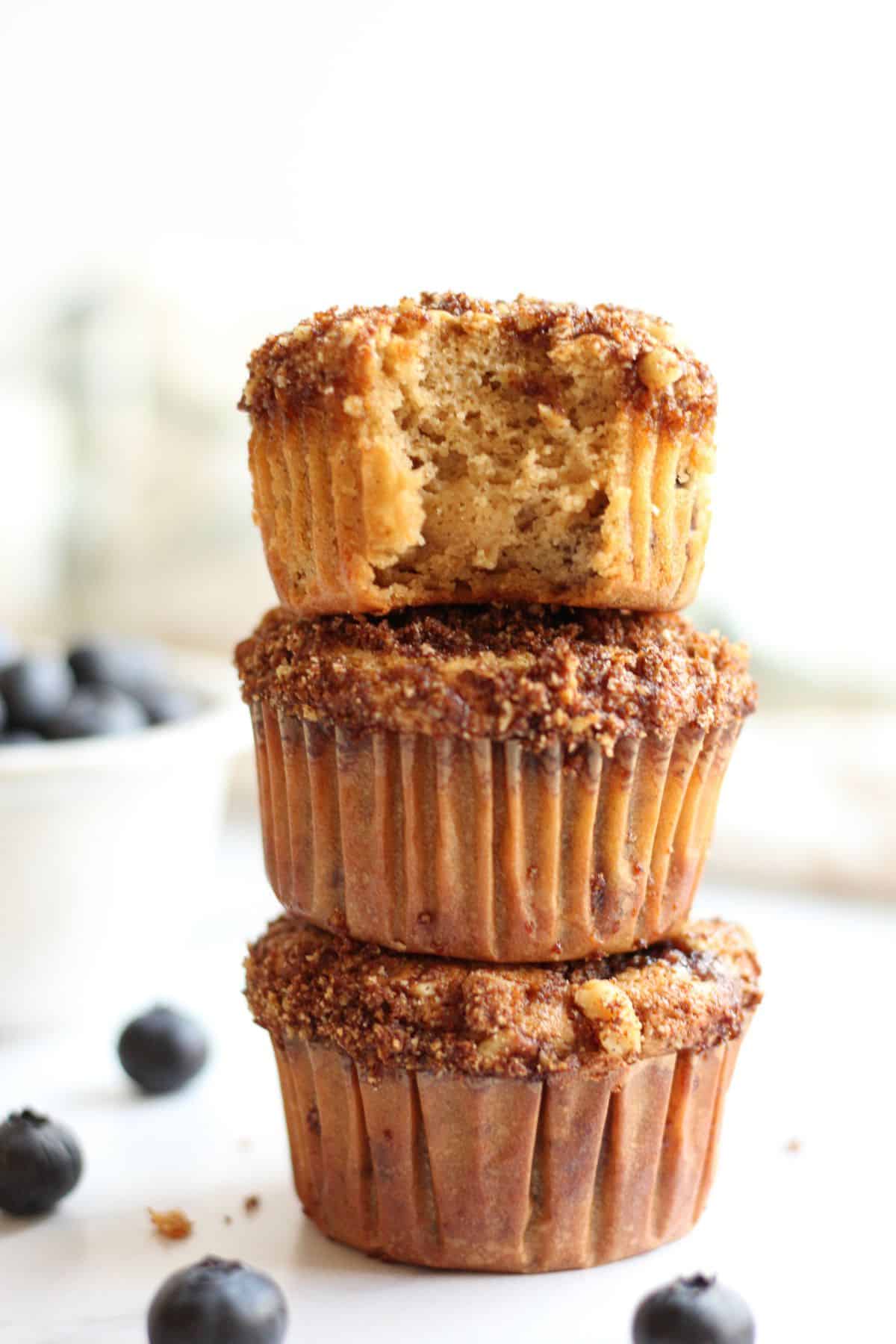 3 gluten and dairy free blueberry muffins stacked on the counter with the top muffin missing a bite to show inside texture.
