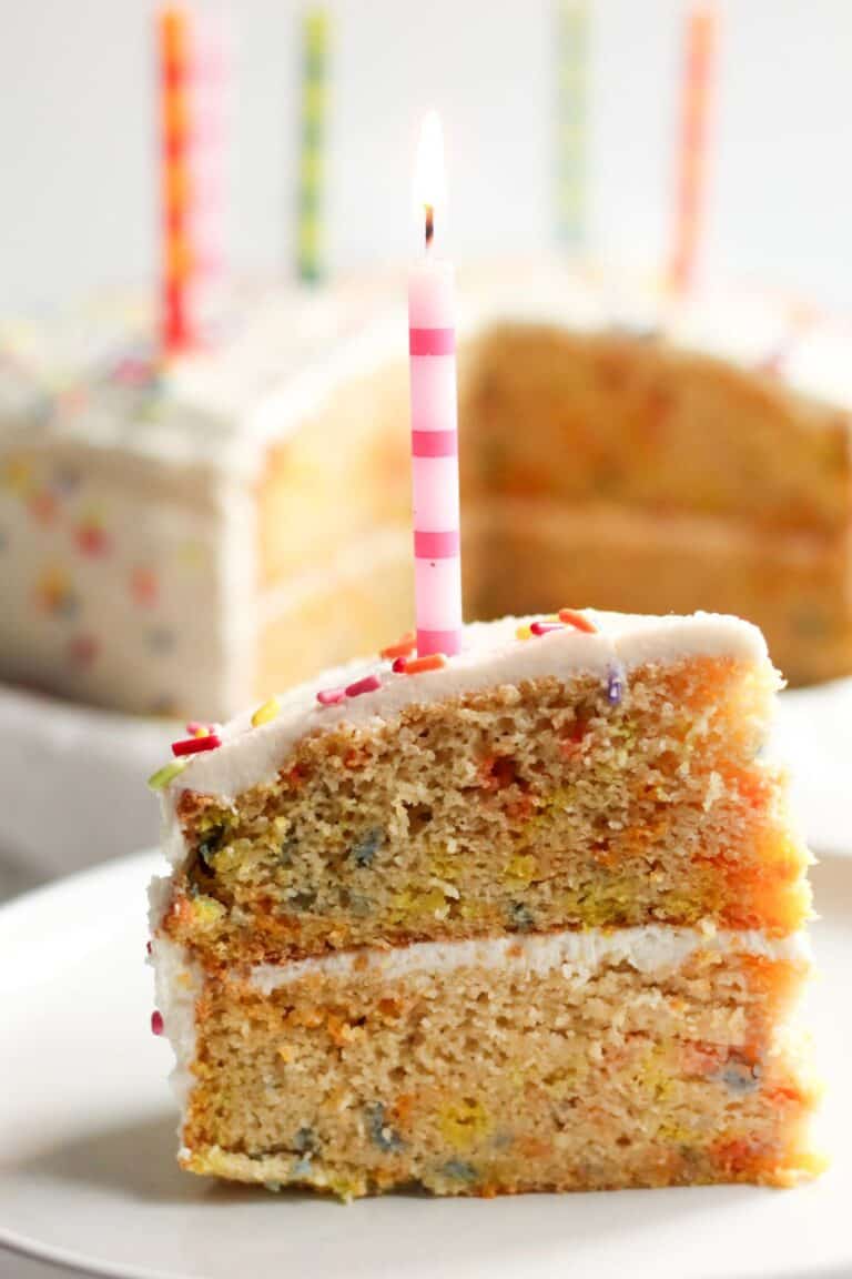 A slice of gluten and dairy free birthday cake being served on a plate with a lit candle on top.