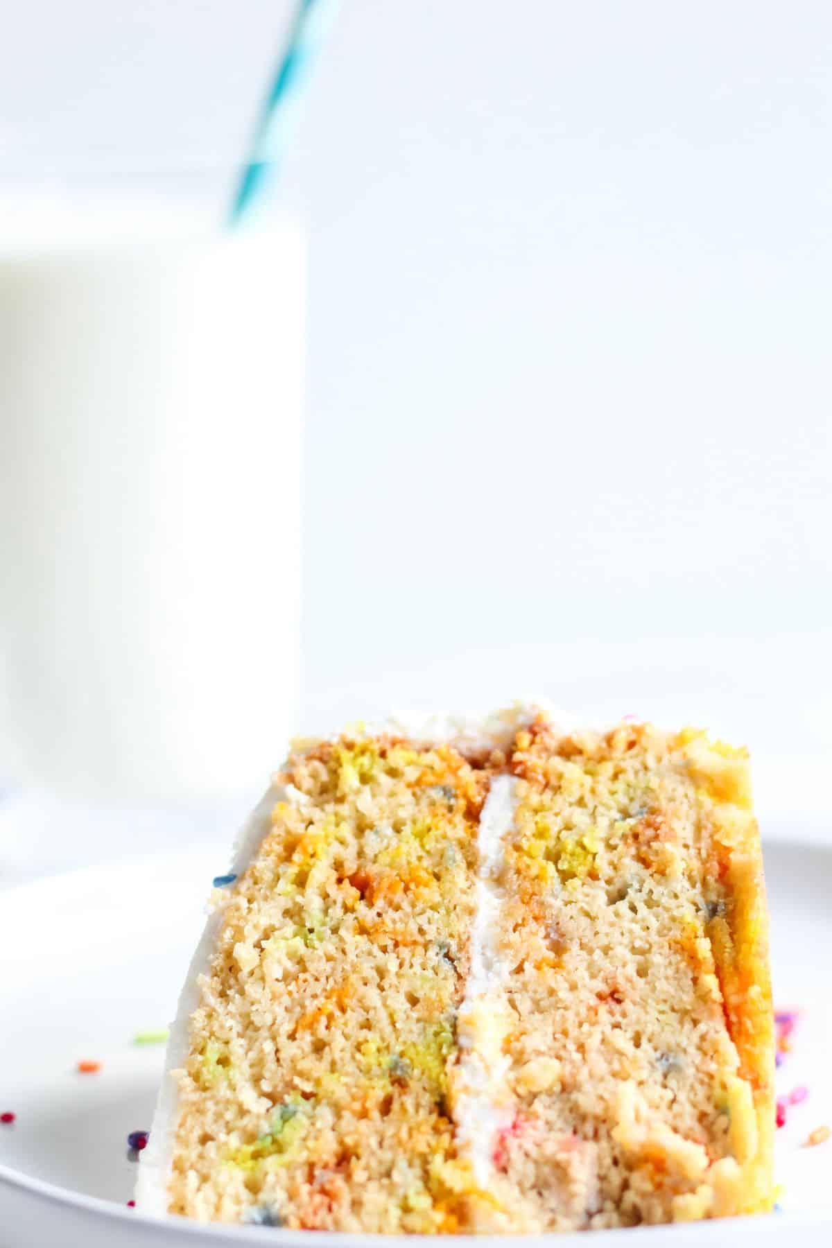 A close up of a slice of gluten and dairy free confetti cake served on a plate with a glass of almond milk.